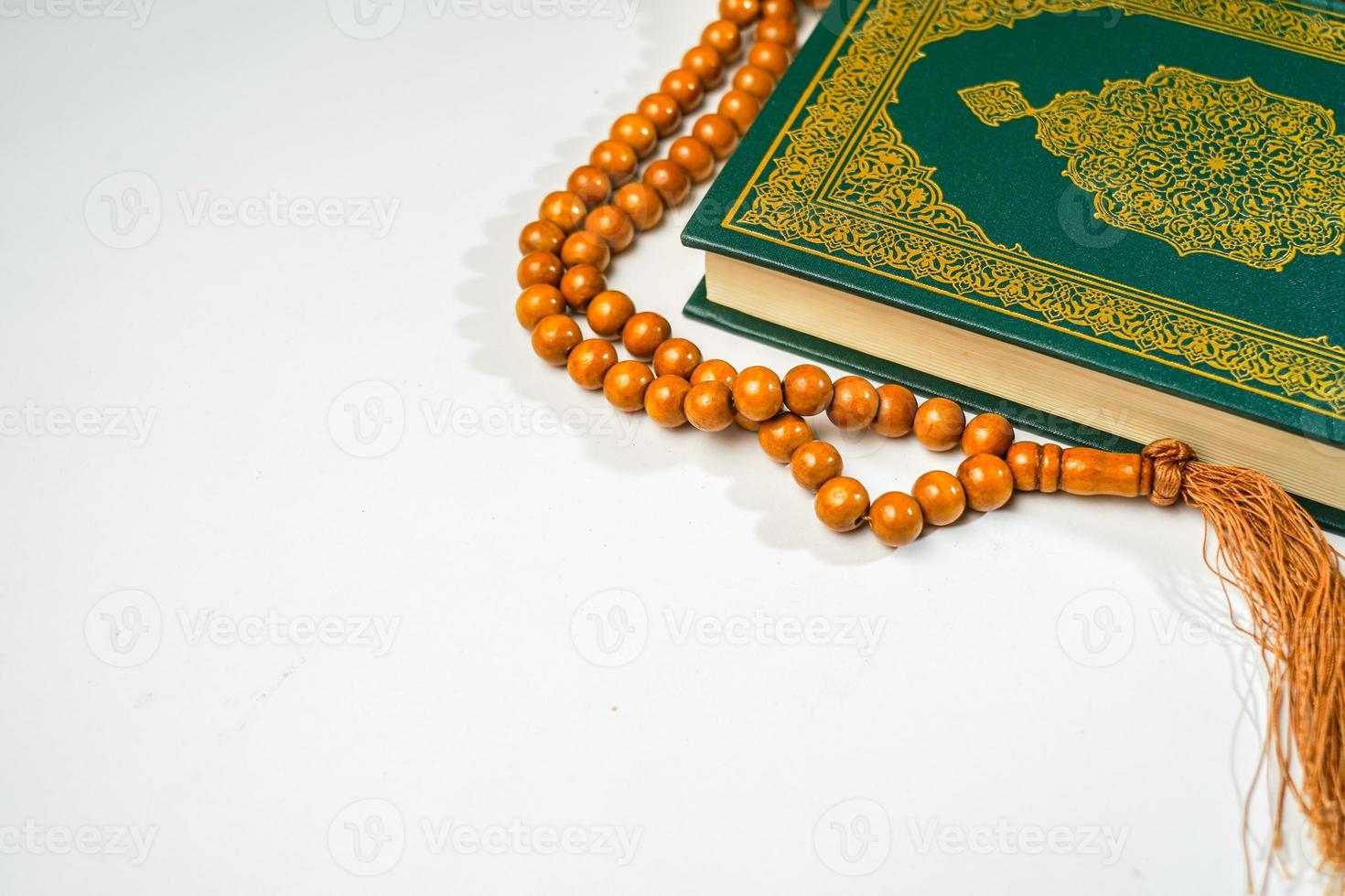 The Holy Al Quran with written arabic calligraphy meaning of Al Quran and rosary beads or tasbih on white background with copy space. photo