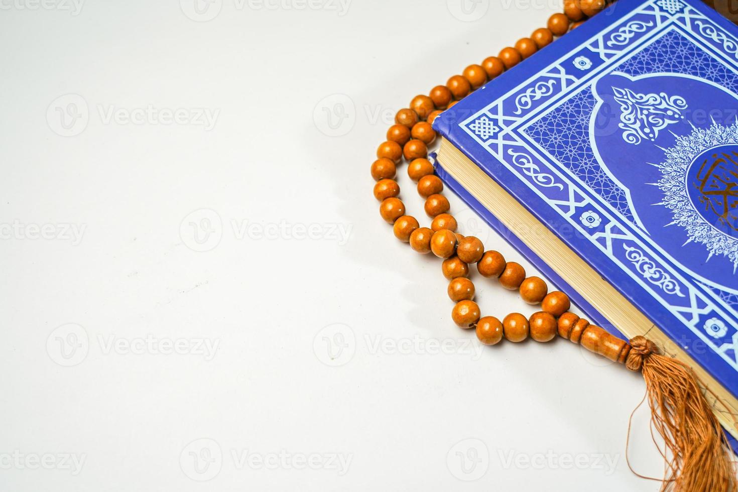 The Holy Al Quran with written arabic calligraphy meaning of Al Quran and rosary beads or tasbih on white background with copy space. photo