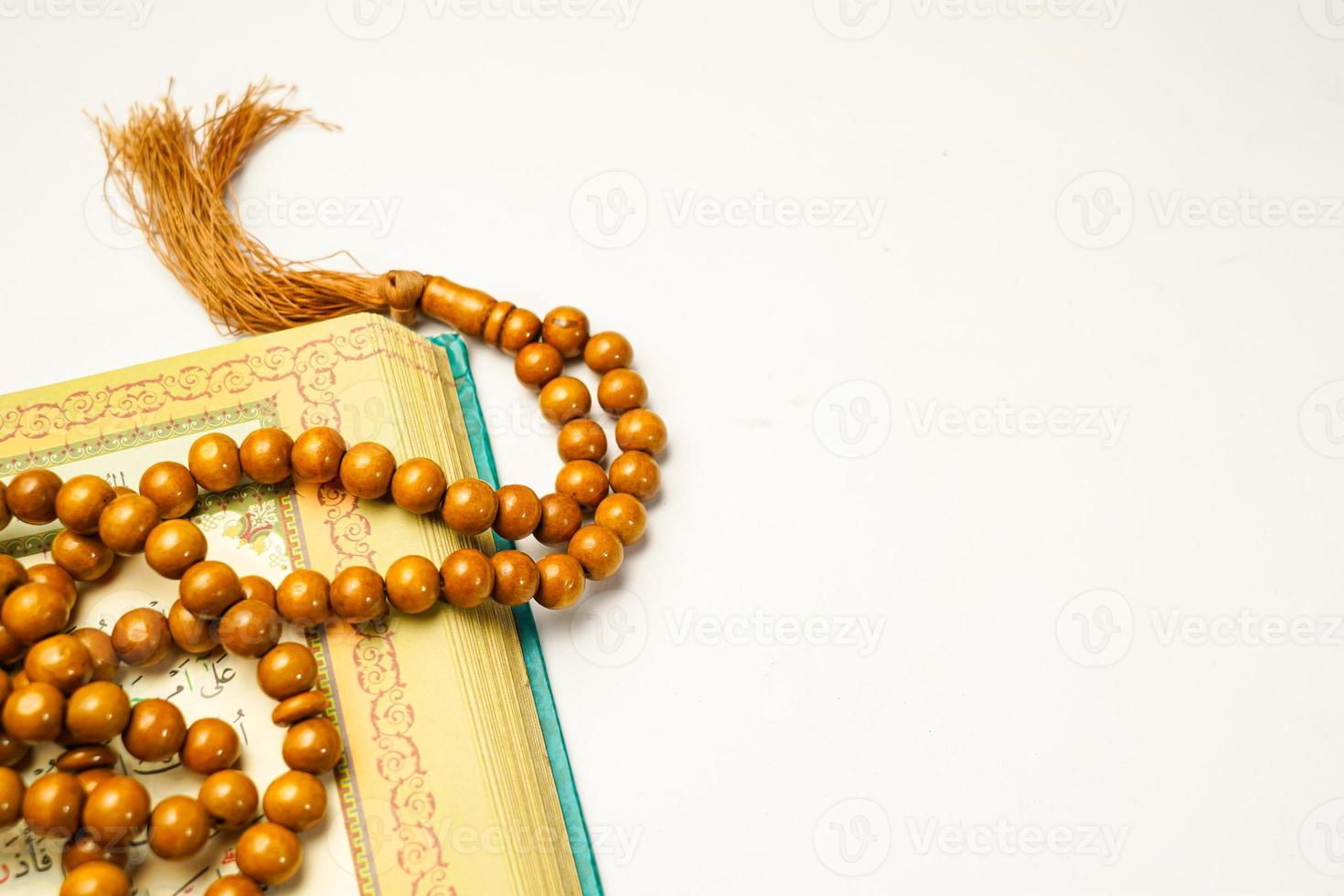 The Holy Al Quran with written arabic calligraphy meaning of Al Quran and rosary beads or tasbih on white background with copy space. photo