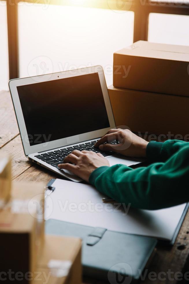 SME entrepreneur Small business entrepreneurs Online selling ideas,Happy Young Asian business owner work on computer and a boxs at home,delivery SME procurement package box deliver to customers, photo