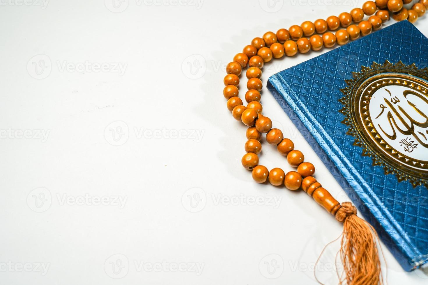 The Holy Al Quran with written arabic calligraphy meaning of Al Quran and rosary beads or tasbih on white background with copy space. photo