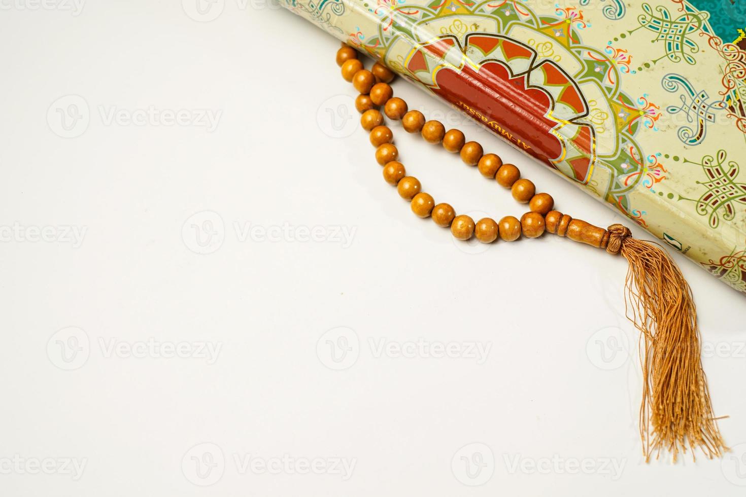 The Holy Al Quran with written arabic calligraphy meaning of Al Quran and rosary beads or tasbih on white background with copy space. photo