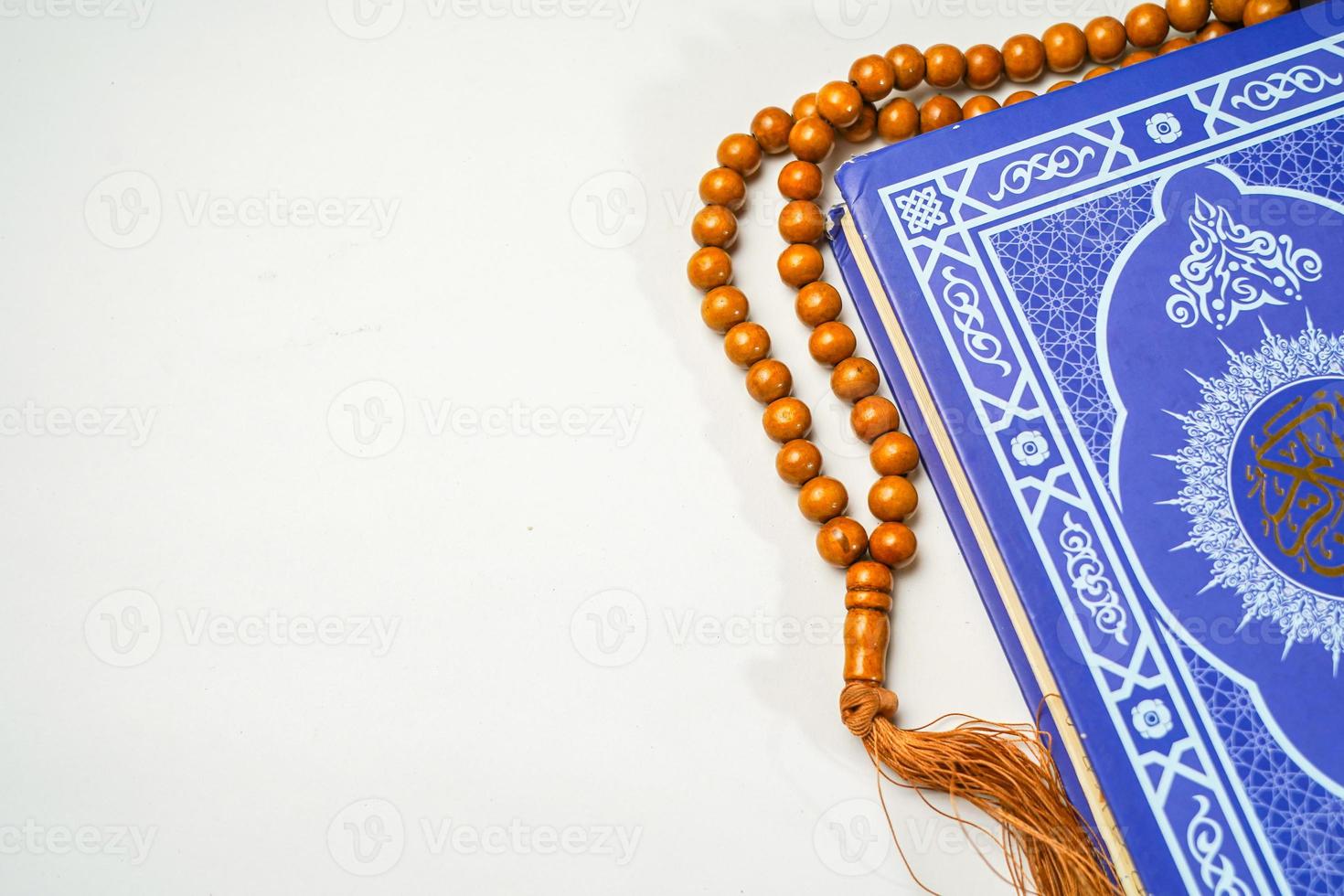 The Holy Al Quran with written arabic calligraphy meaning of Al Quran and rosary beads or tasbih on white background with copy space. photo
