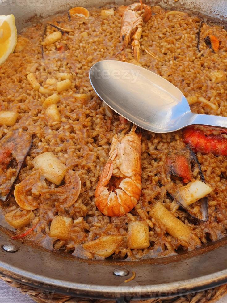 caliente Español paella con Mariscos y langostinos y un cuchara foto