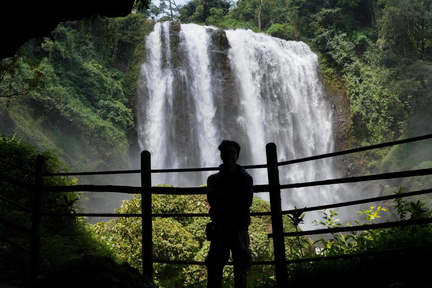 Silhouette man on the cave in front of great water fall, Semarang Central Java. The photo is suitable to use for adventure content media, nature poster and forest background.