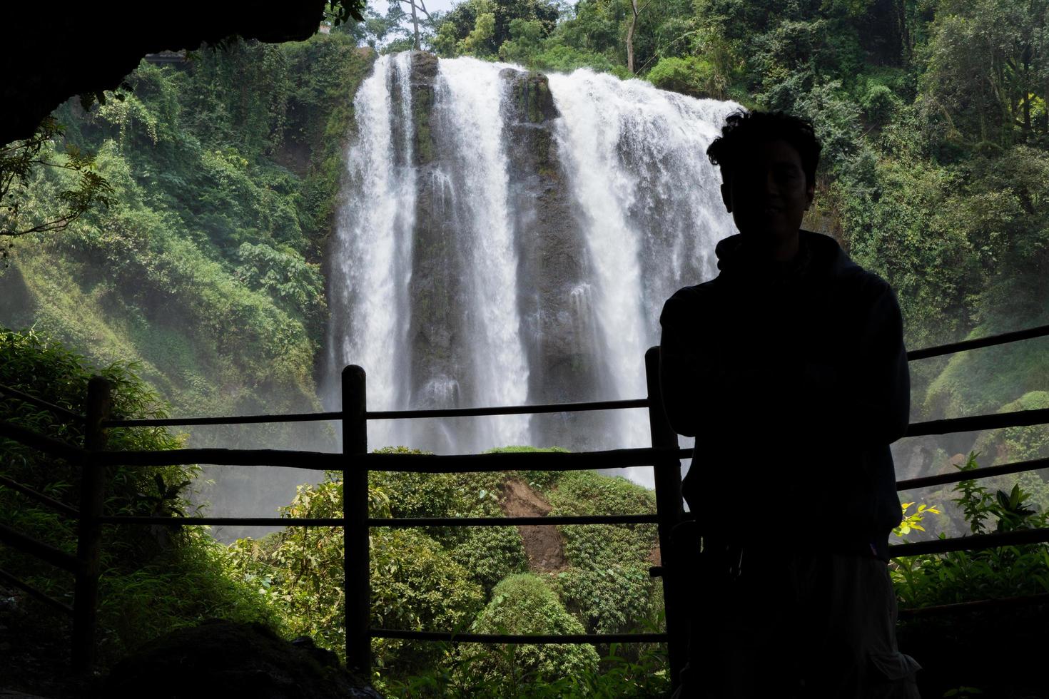 Silhouette man on the cave in front of great water fall, Semarang Central Java. The photo is suitable to use for adventure content media, nature poster and forest background.