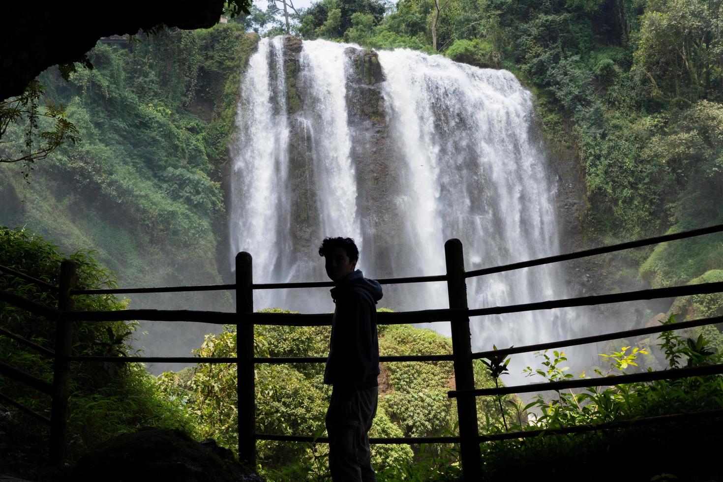 Silhouette man on the cave in front of great water fall, Semarang Central Java. The photo is suitable to use for adventure content media, nature poster and forest background.