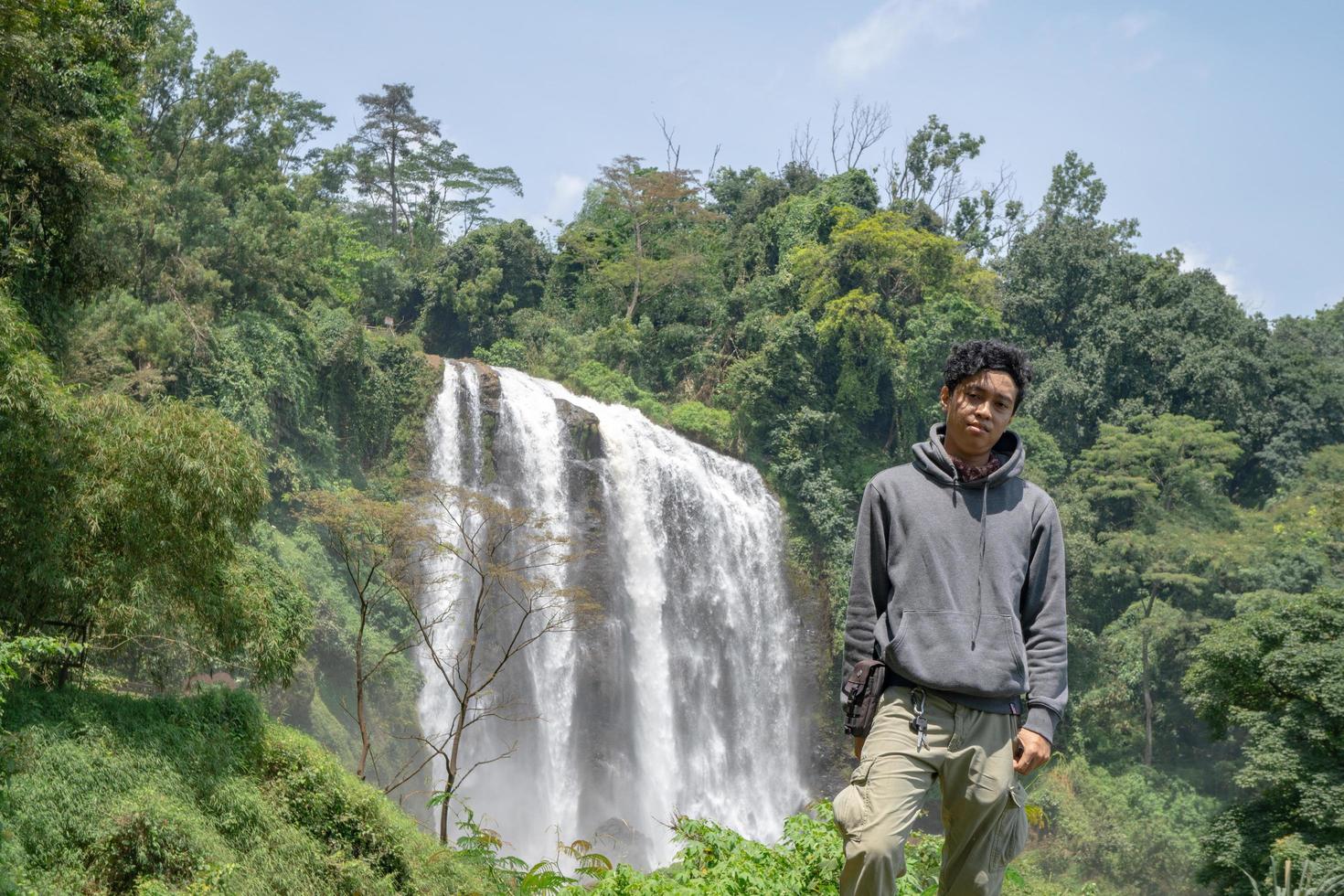 Man stand wear hoody in front of the great water fall with hand reel, Semarang central Java. The photo is suitable to use for adventure content media, nature poster and forest background.