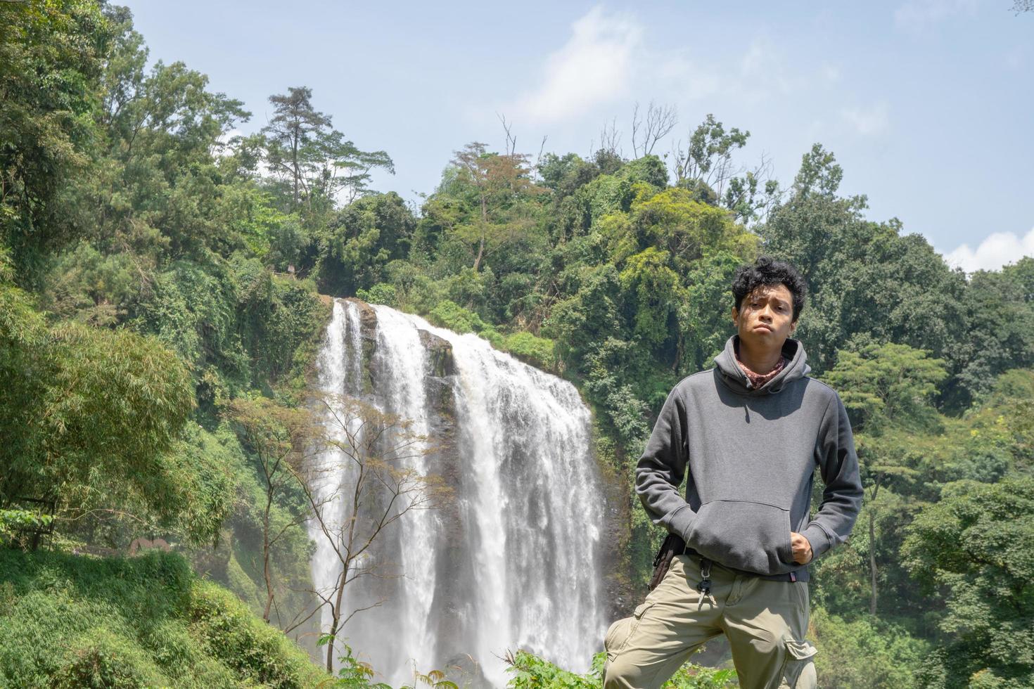 Man stand wear hoody in front of the great water fall with hand reel, Semarang central Java. The photo is suitable to use for adventure content media, nature poster and forest background.