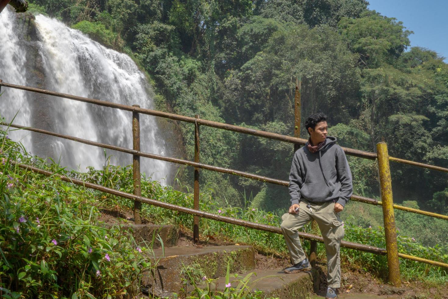 Man stand wear hoody in front of the great water fall with hand reel, Semarang central Java. The photo is suitable to use for adventure content media, nature poster and forest background.