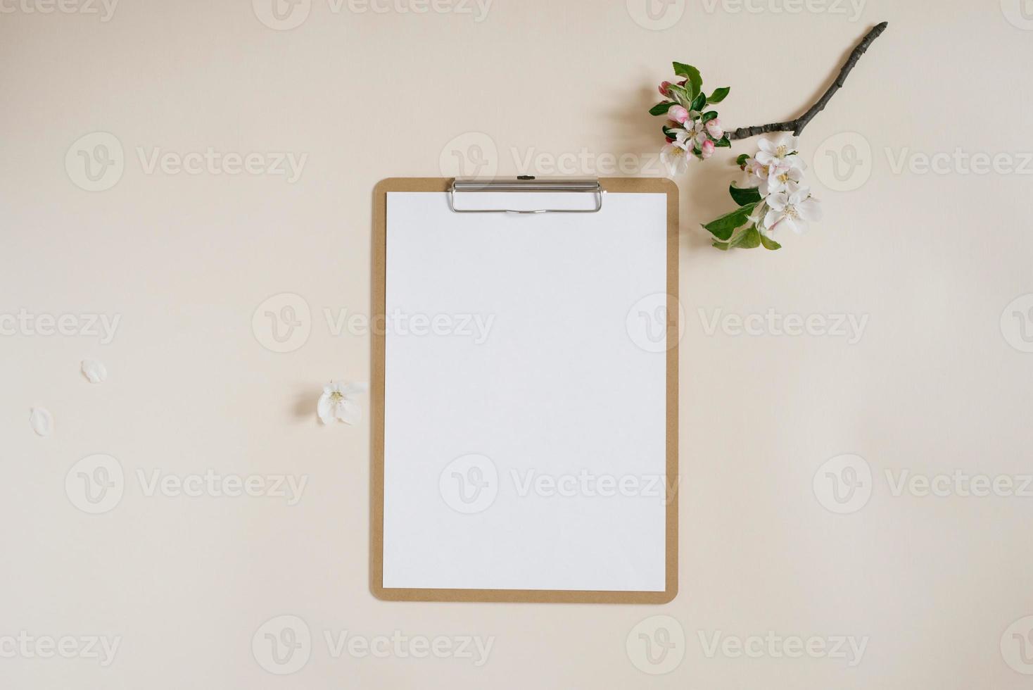 Blank sheet of paper with clipboard for tablet with copy space for copy. Beautiful home office table table workspace with fresh apple tree flowers. Flat lay, top view art concept photo