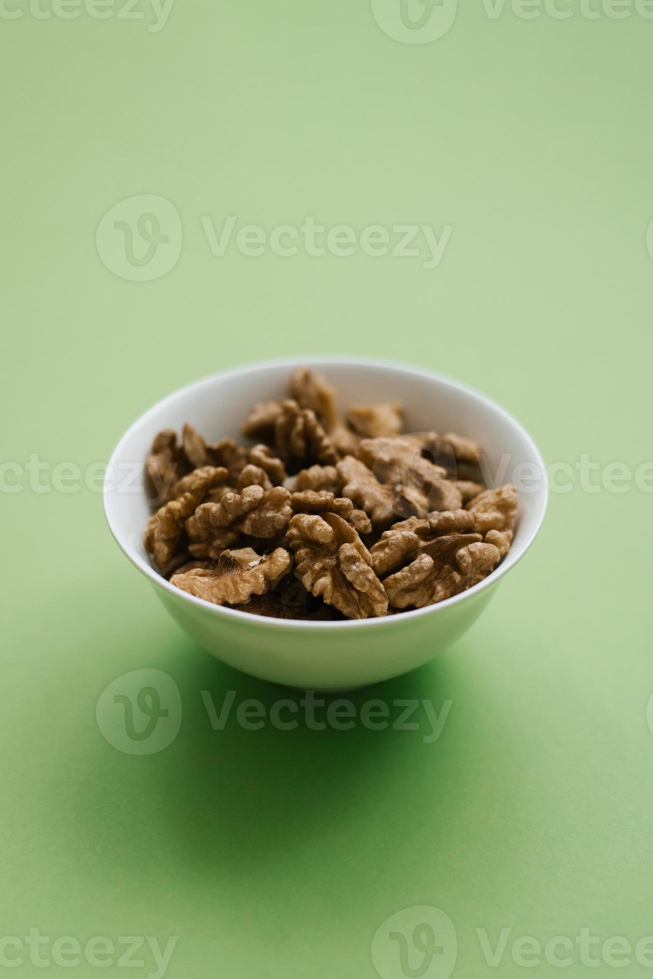 Peeled walnuts on a white plate on a green background with a copy space