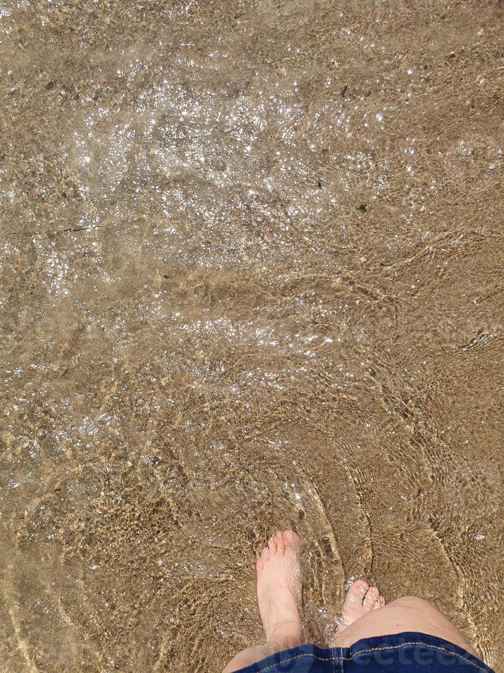 mujer pies inmerso en el mar agua a el playa en un soleado calentar día foto