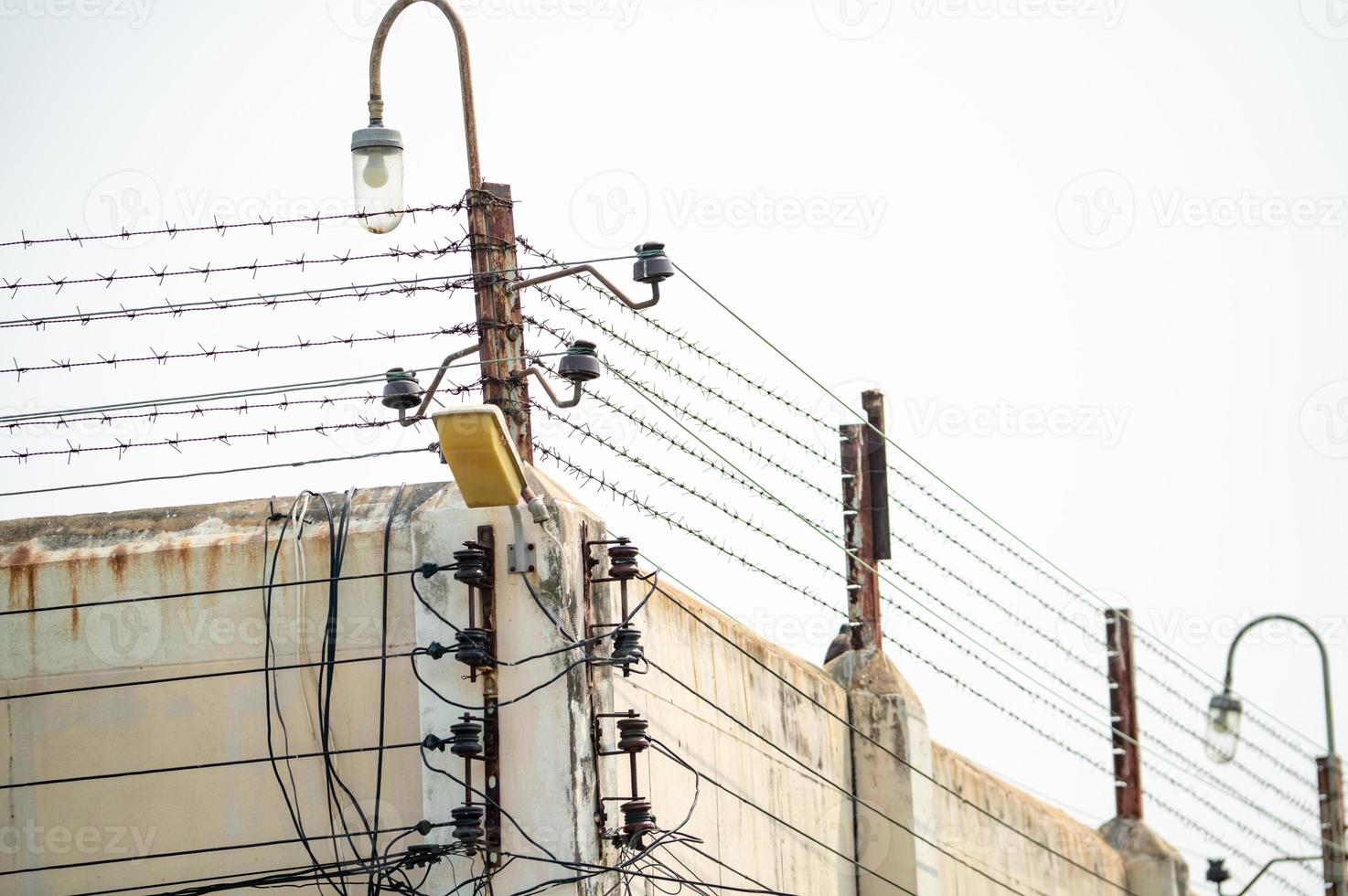 Prison security electric fence and high concrete wall. Prison high voltage fence. Barbed wire security fence. Razor wire jail fence. Prison for arrest criminals or terrorists. Military zone concept. photo
