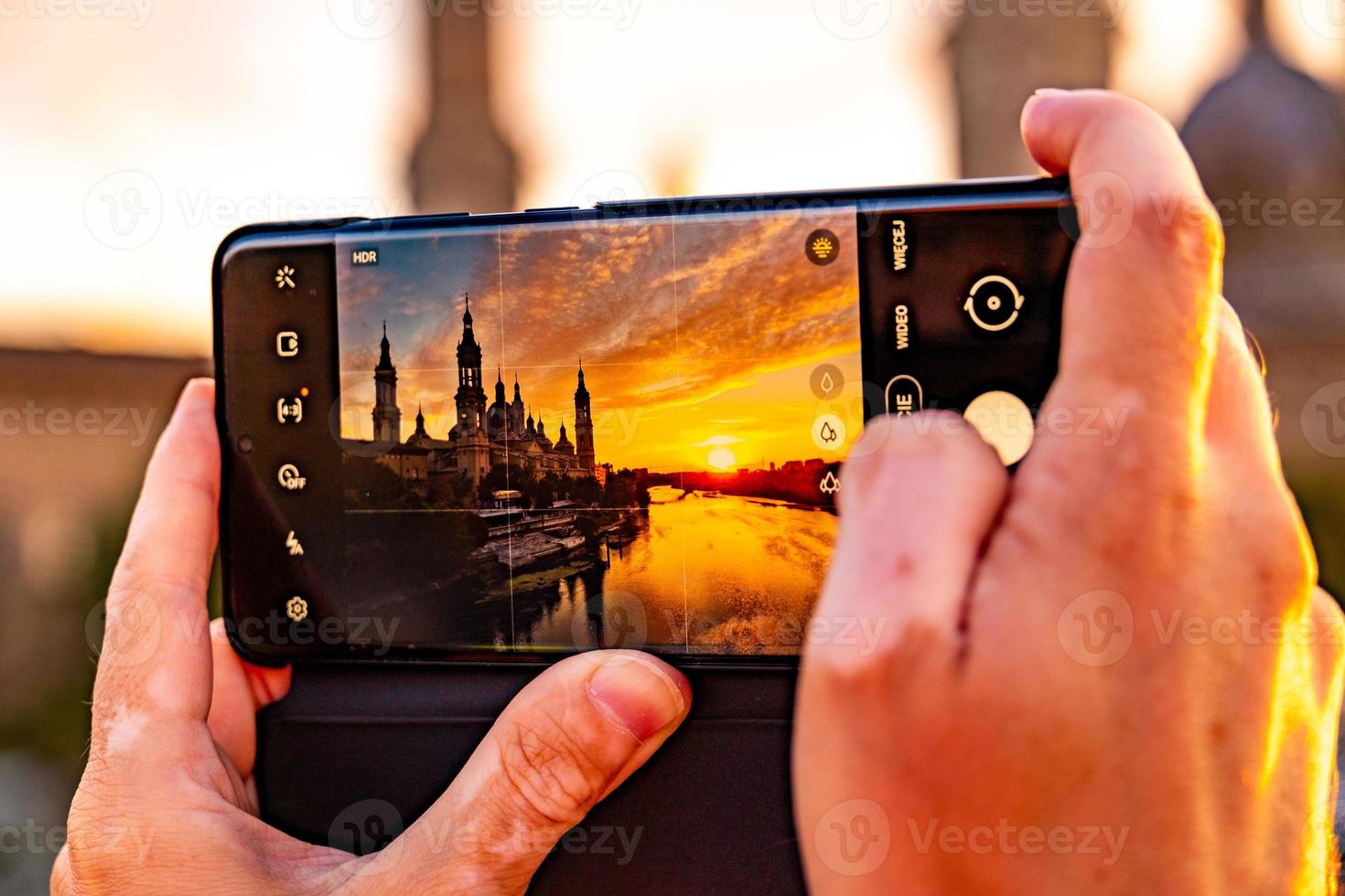 picturesque sunset on a summer day in the city of Zaragoza in Spain with a view of the river and the cathedral while taking a photo with a mobile phone