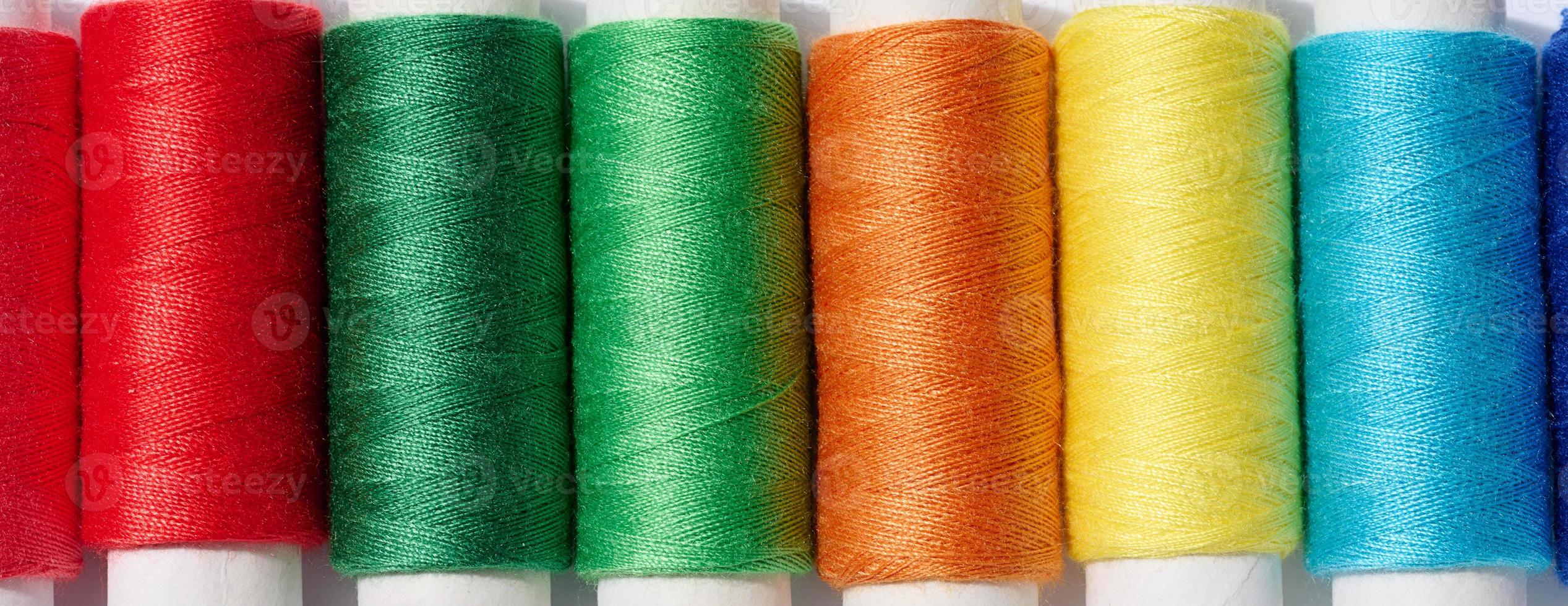 Multicolored spools of sewing threads on a white background, top view photo