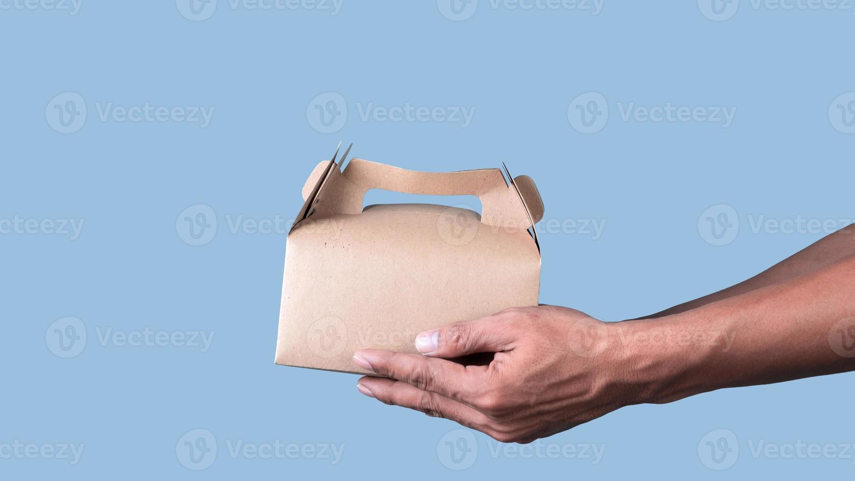 Male hand holding brown ecological package box made of natural cardboard on light blue background. Packaging, shopping, Food delivery concept photo