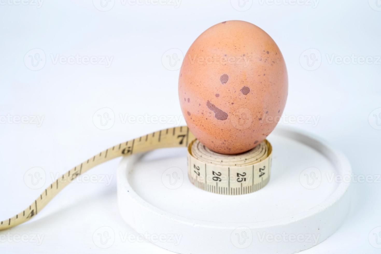 Chicken egg and measuring tape on white round coaster with copy space for text. Concept of diet and healthy living photo