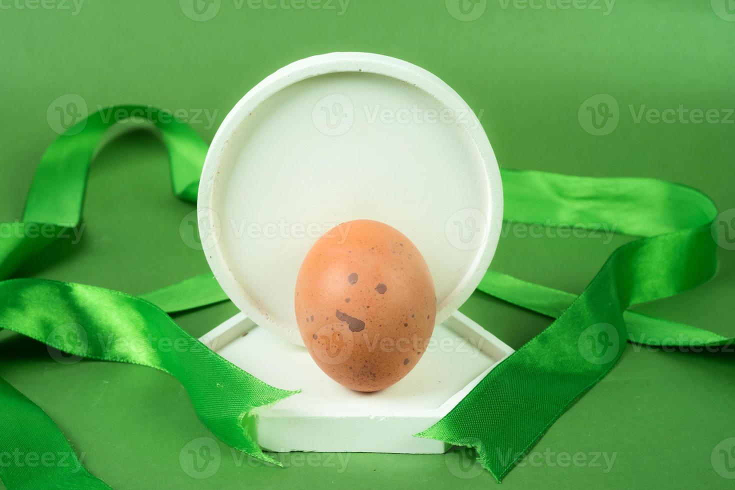 Chicken eggs on white podium with green ribbon on green background. photo