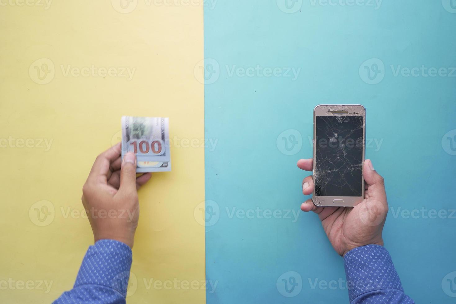 man hand holding broken smart phone and cash on table photo