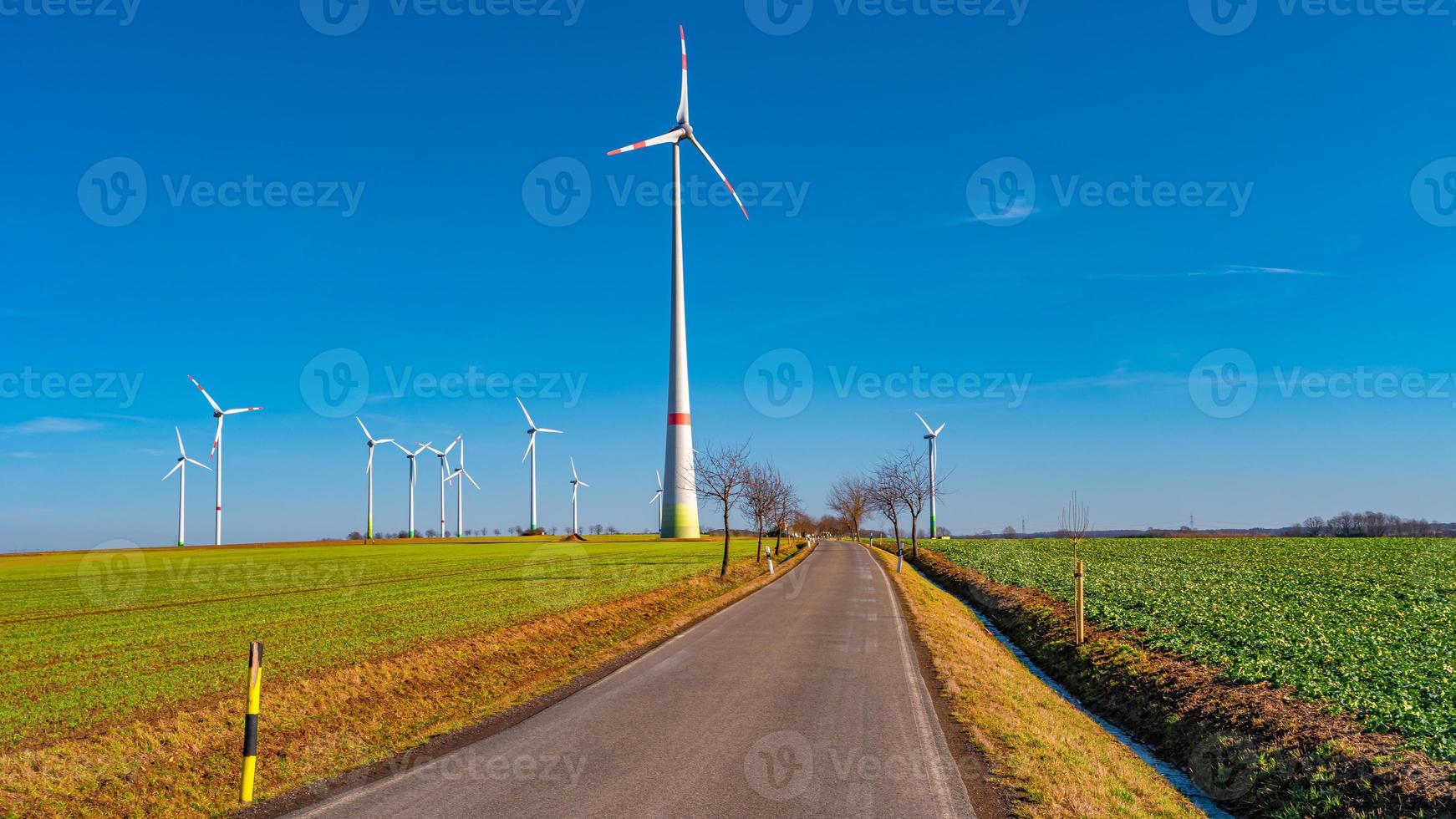 View over beautiful farm landscape with early spring agriculture field, wind turbines to produce green energy and a lonely road near Mittweida, Germany, at blue sunny sky. photo