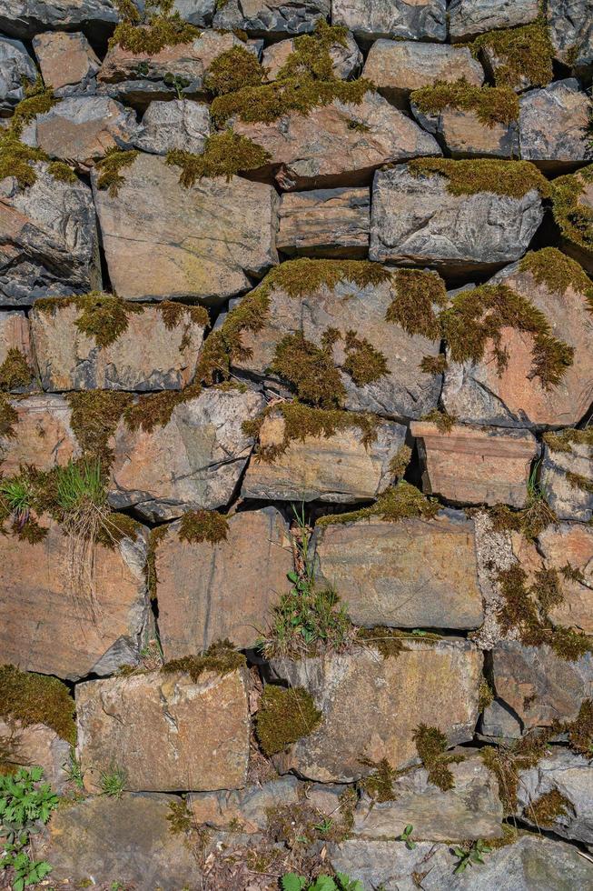 Pattern of ancient bricks and stones at old middle age fortress wall covered with moss, grass and lichen, as a background, closeup, details. photo
