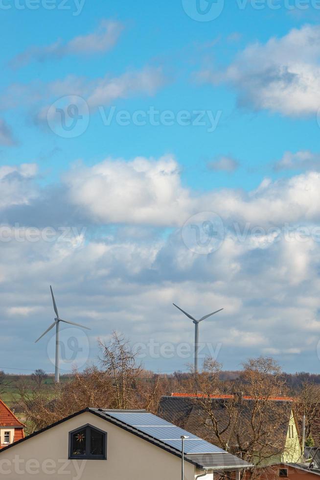 View over beautiful farm landscape with early spring agriculture field, wind turbines to produce green energy and a solar panels at the house roof in Mittweida, Germany, at blue sunny sky photo