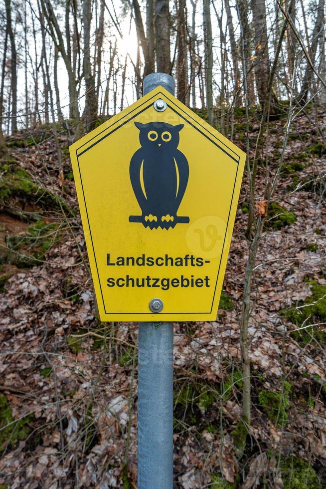 Trail stand post in forest with a sign of an owl bird at yellow background and note that it is protected landscape written in German photo