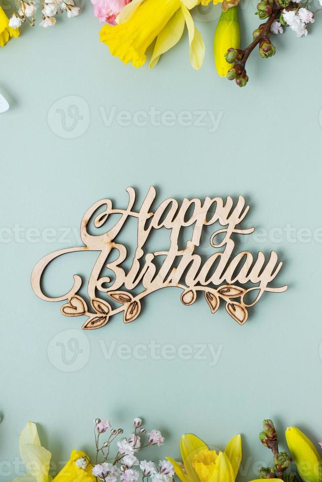 Happy birthday text with spring flowers flat lay frame composition on colored background photo