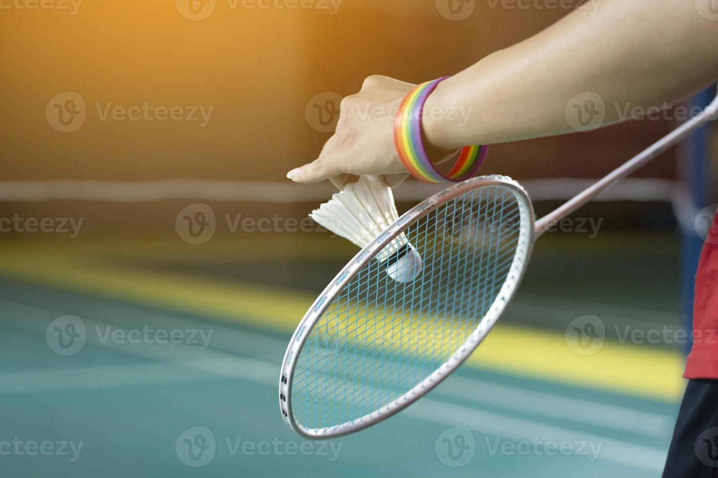 Badminton player wears rainbow wristbands and holding racket and white shuttlecock in front of the net before serving it to player in another side of the court, concept for LGBT people activities. photo