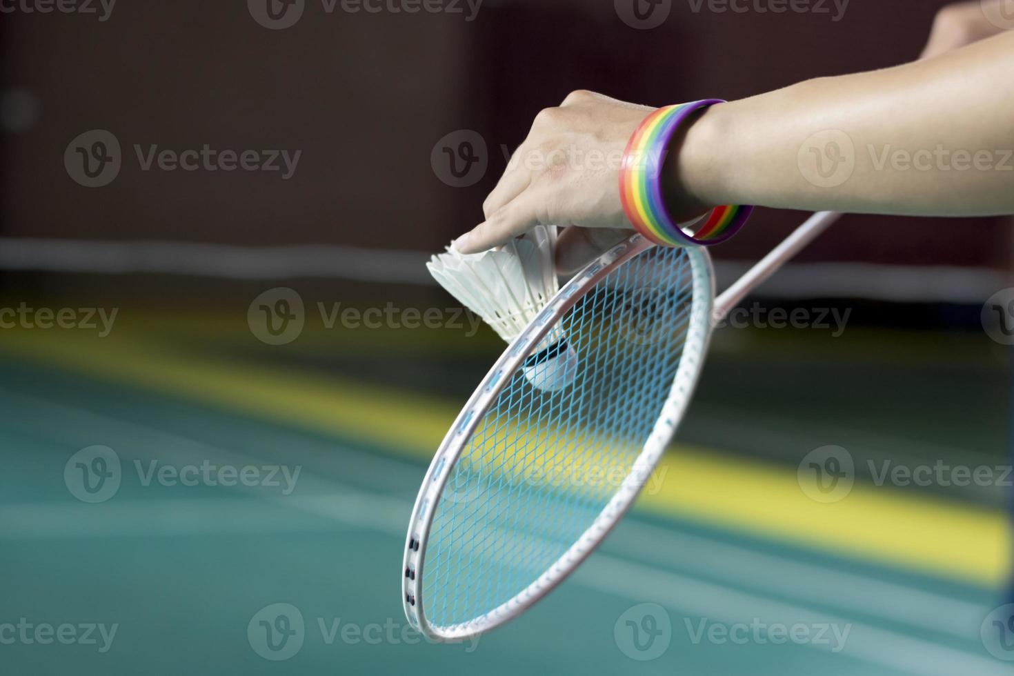 Badminton player wears rainbow wristbands and holding racket and white shuttlecock in front of the net before serving it to player in another side of the court, concept for LGBT people activities. photo