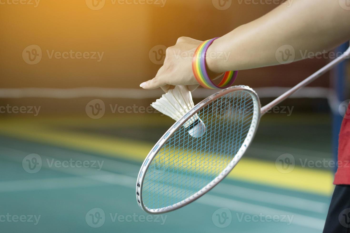 Badminton player wears rainbow wristbands and holding racket and white shuttlecock in front of the net before serving it to player in another side of the court, concept for LGBT people activities. photo
