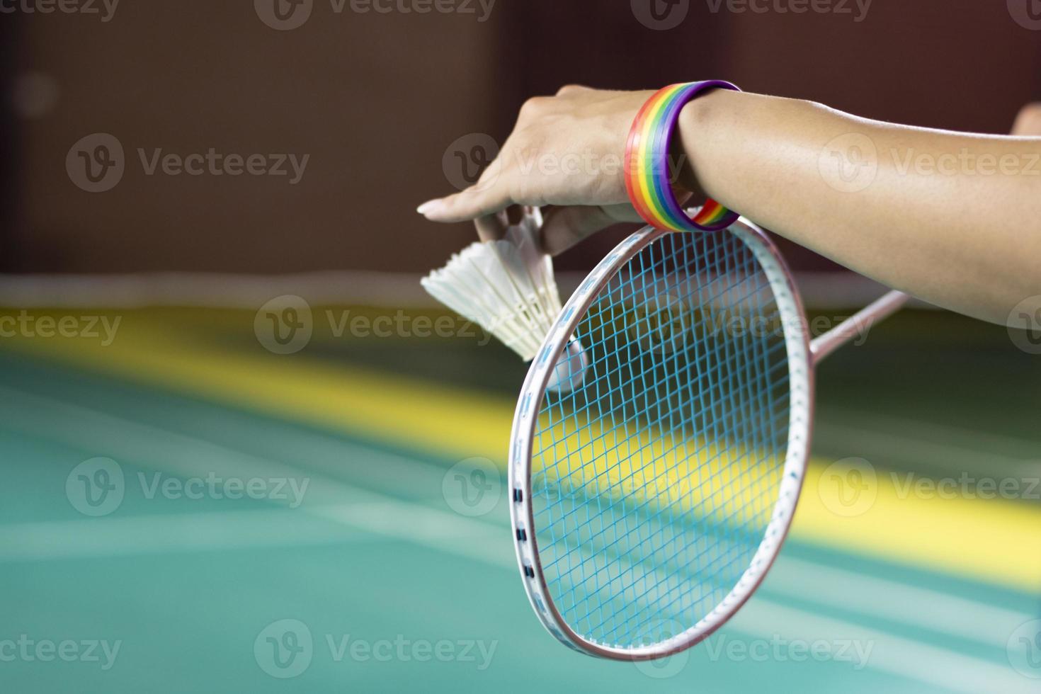 Badminton player wears rainbow wristbands and holding racket and white shuttlecock in front of the net before serving it to player in another side of the court, concept for LGBT people activities. photo