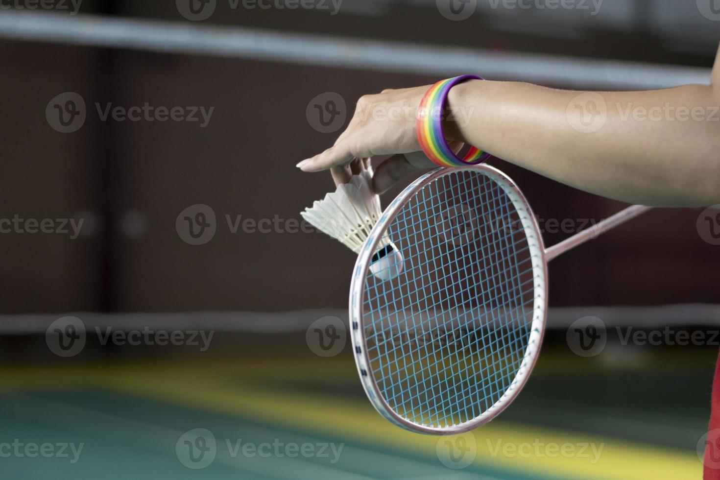 Badminton player wears rainbow wristbands and holding racket and white shuttlecock in front of the net before serving it to player in another side of the court, concept for LGBT people activities. photo