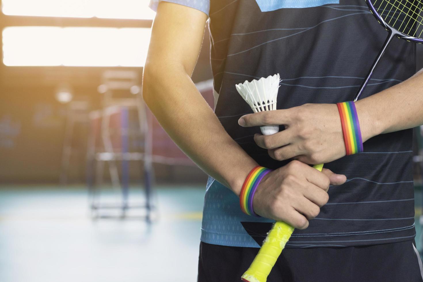 Badminton player wears rainbow wristbands and holding racket and white shuttlecock in front of the net before serving it to player in another side of the court, concept for LGBT people activities. photo