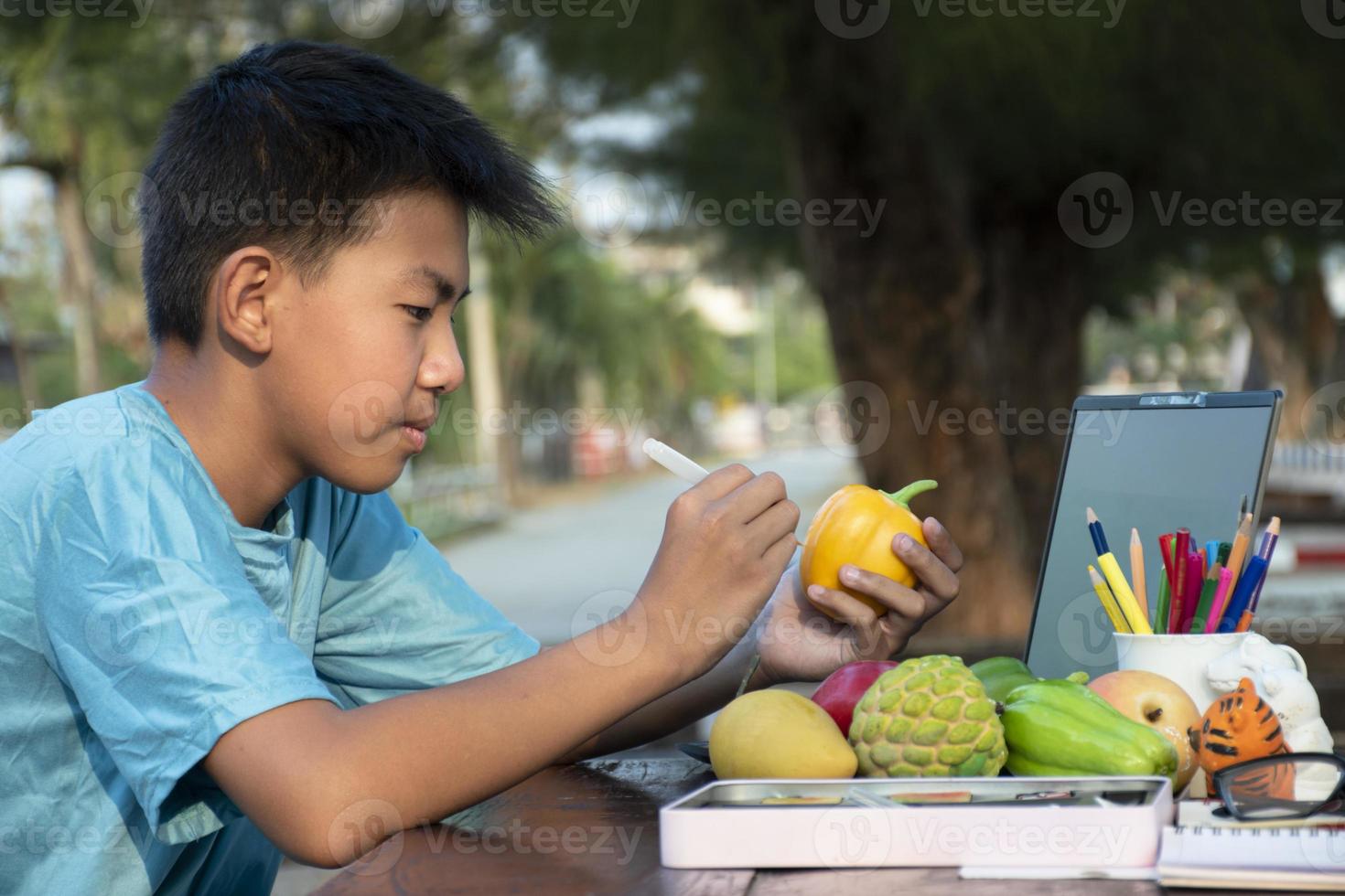Asian boy holds paintbrush and yellow bell pepper which molded from plaster, coloring and painting outer surface with same color during his free times, idea for hobby and art learning. photo