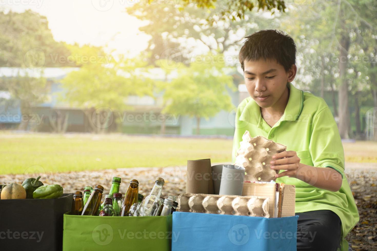 Young asian boy sorting various garbages and putting them into the boxes infront of him in the park, nature care and environment love concept. photo