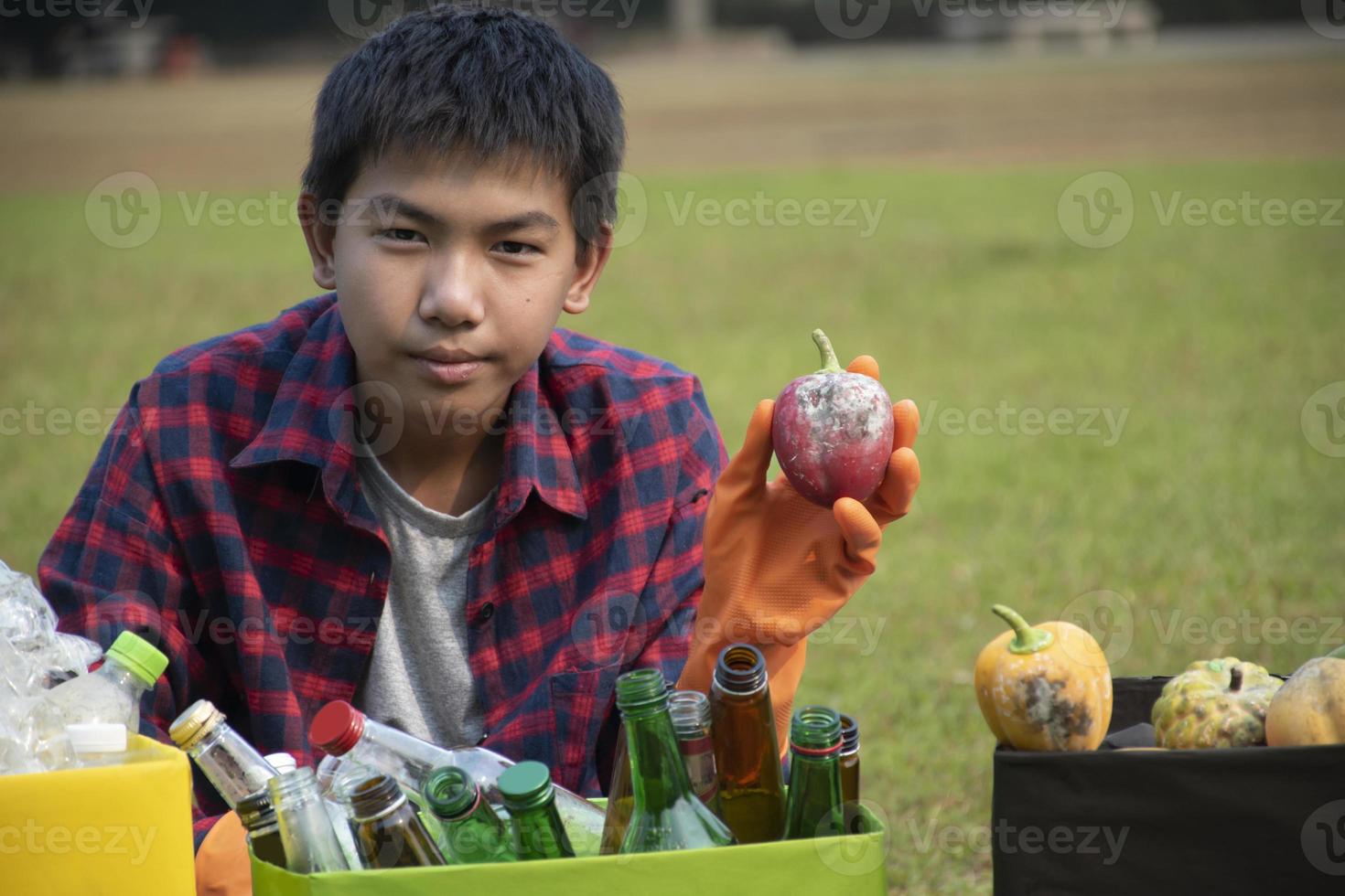 Young asian boy sorting various garbages and putting them into the boxes infront of him in the park, nature care and environment love concept. photo