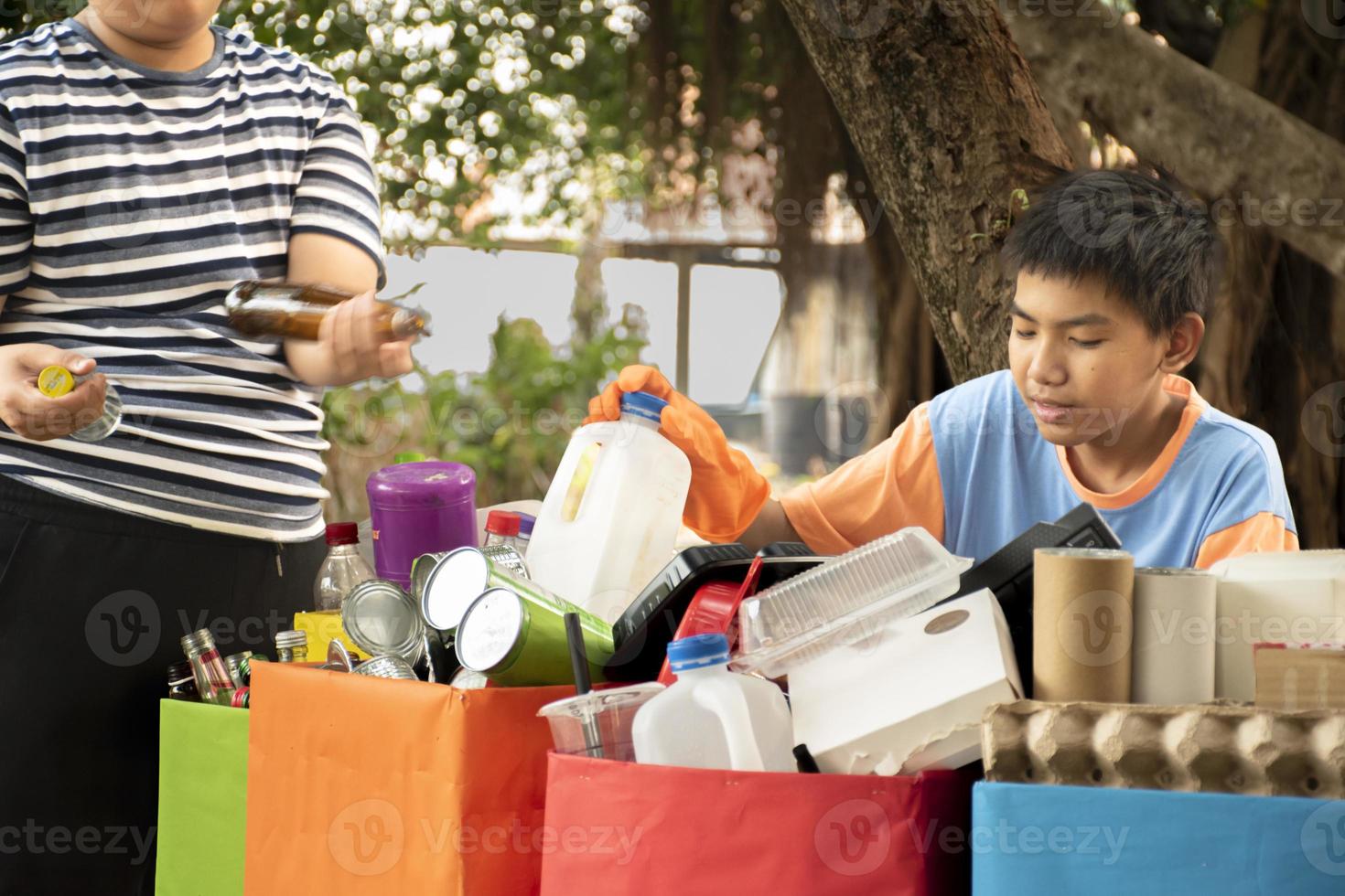 Young asian boy sorting various garbages and putting them into the boxes infront of him in the park, nature care and environment love concept. photo