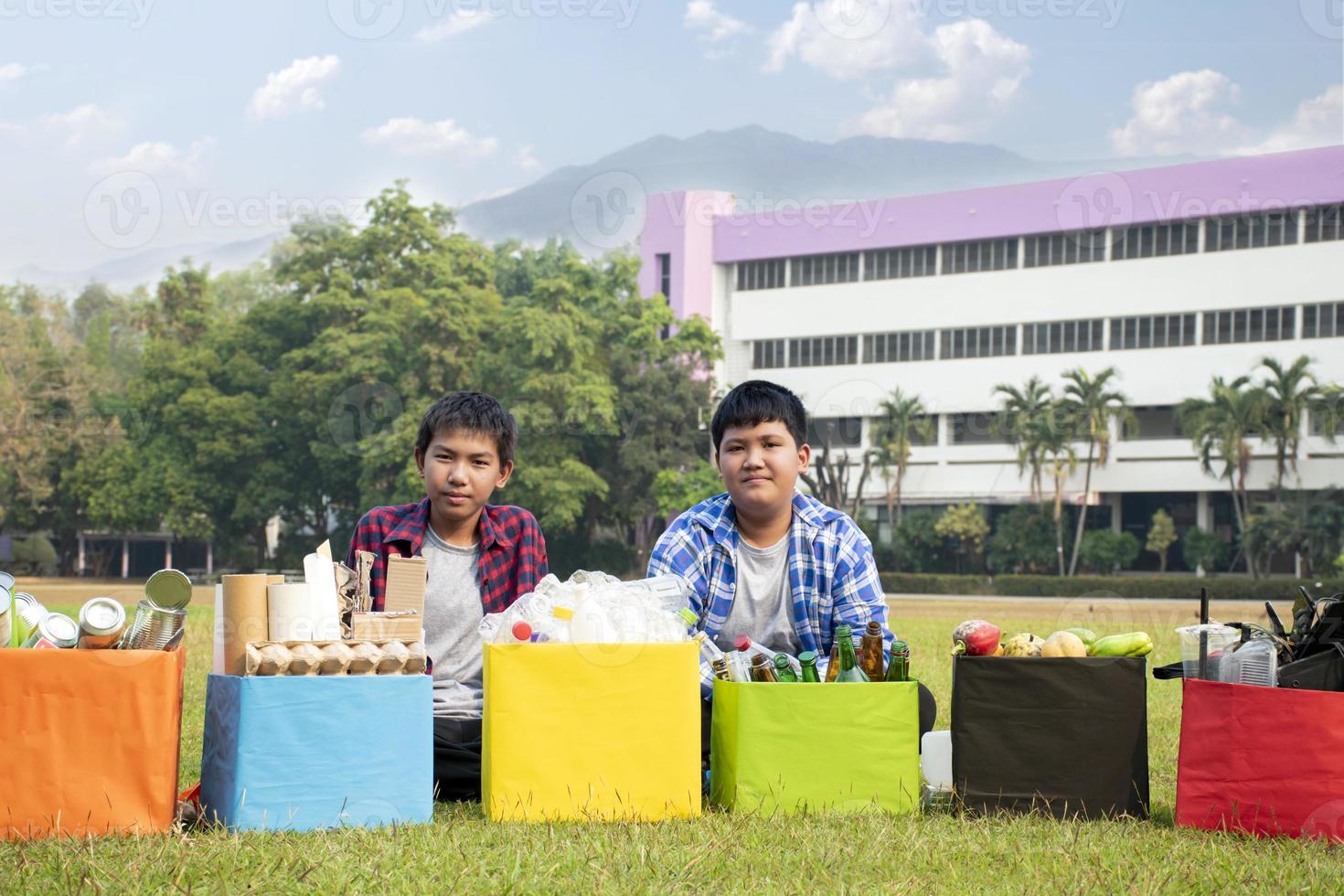 Young asian boy sorting various garbages and putting them into the boxes infront of him in the park, nature care and environment love concept. photo