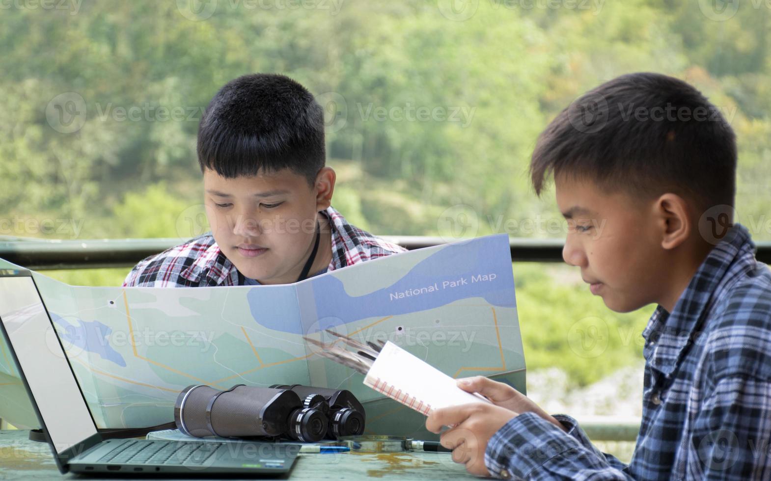 Asian boys using binoculars to do the birdwatching in tropical forest during summer camp, idea for learning creatures, wildlife animals and insects outside the classroom. photo