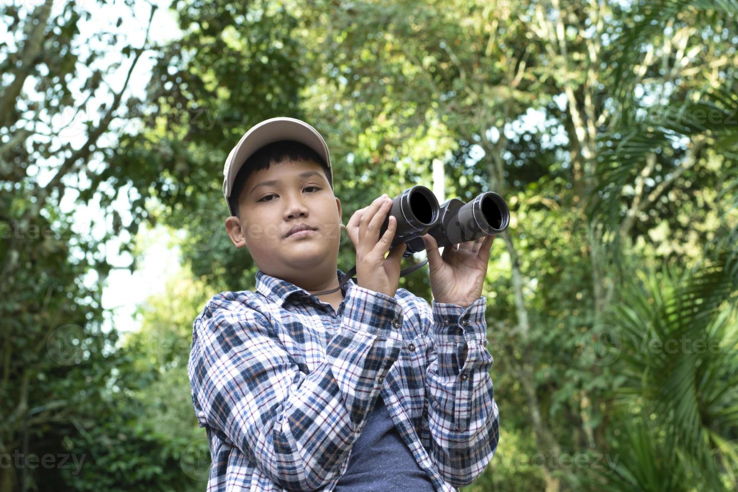 Asian boys using binoculars to do the birdwatching in tropical forest during summer camp, idea for learning creatures, wildlife animals and insects outside the classroom. photo