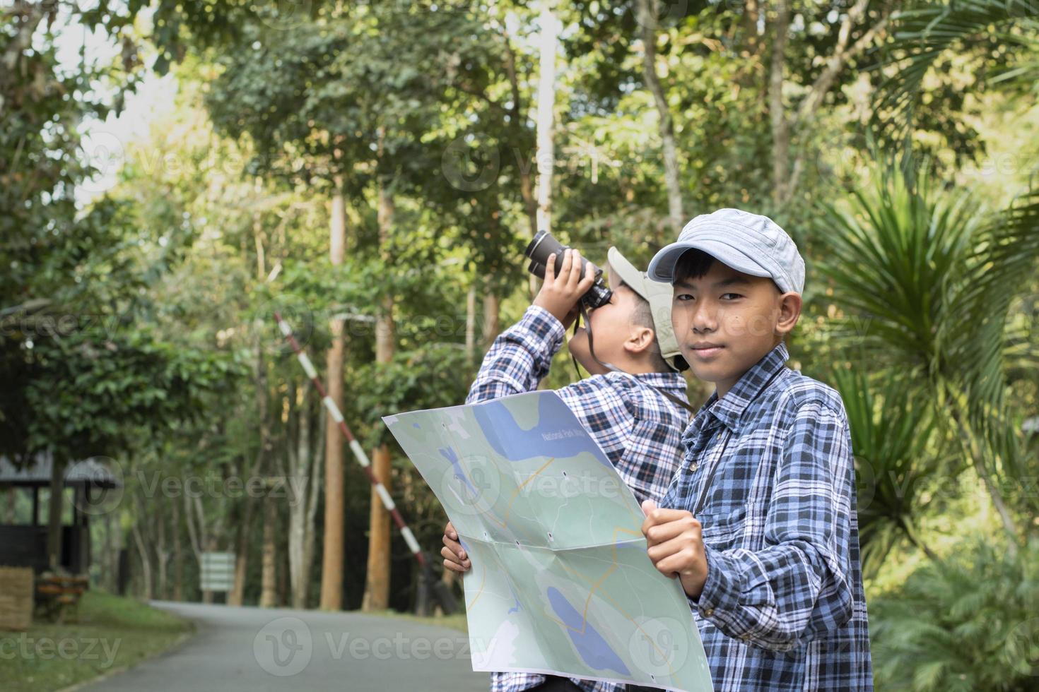 Asian boys using binoculars to do the birdwatching in tropical forest during summer camp, idea for learning creatures, wildlife animals and insects outside the classroom. photo