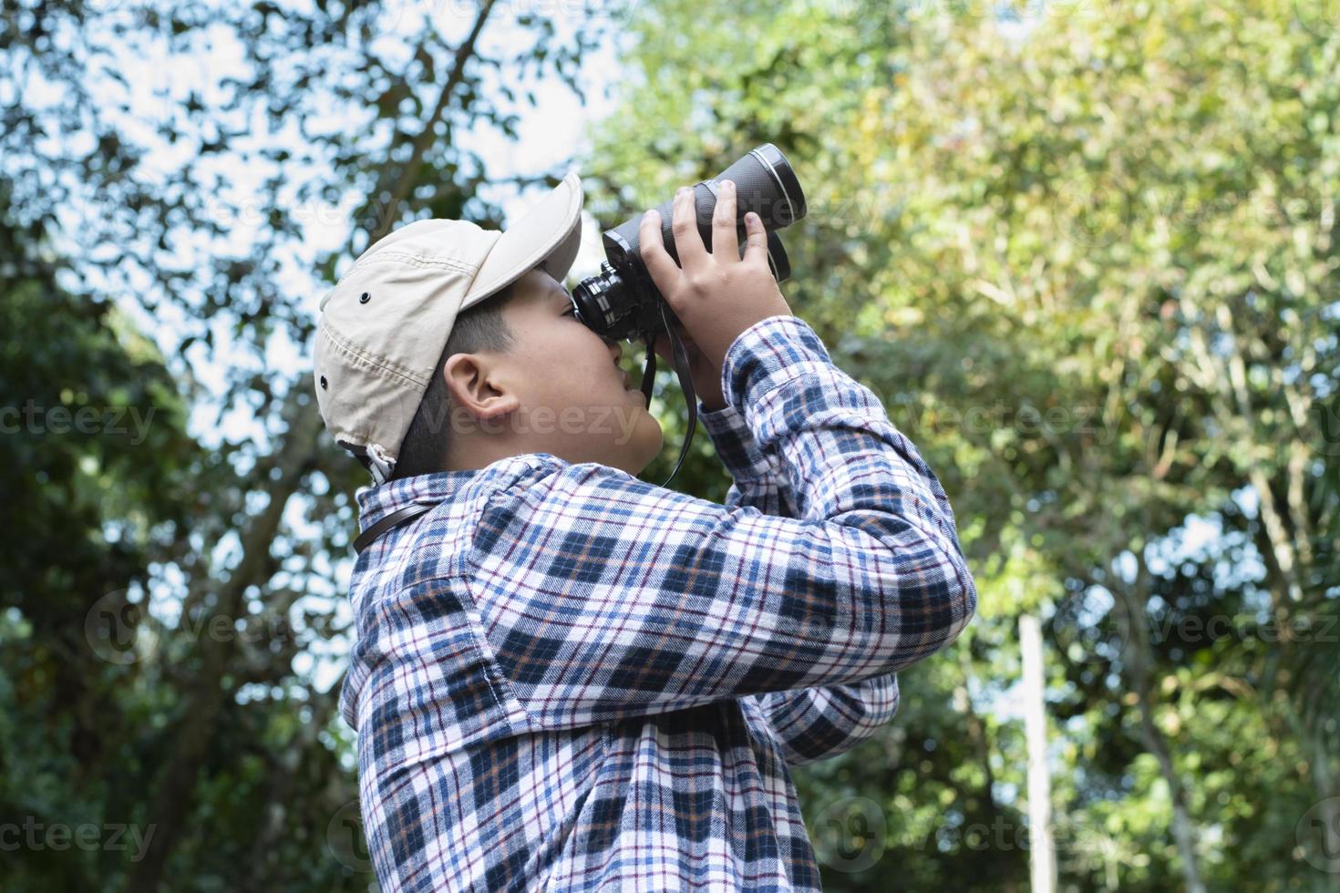 Asian boys using binoculars to do the birdwatching in tropical forest during summer camp, idea for learning creatures, wildlife animals and insects outside the classroom. photo