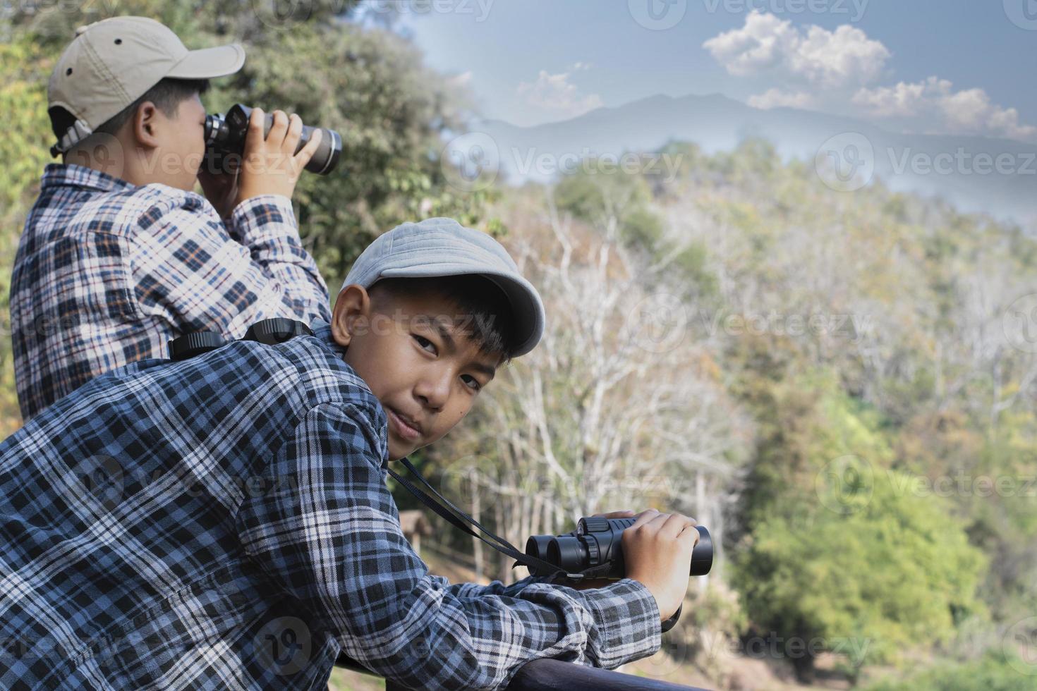 asiático Niños utilizando prismáticos a hacer el ornitología en tropical bosque durante verano acampar, idea para aprendizaje criaturas, fauna silvestre animales y insectos fuera de el aula. foto