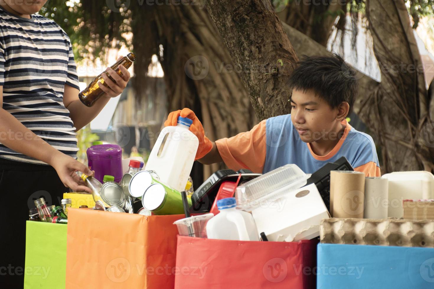 Young asian boy sorting various garbages and putting them into the boxes infront of him in the park, nature care and environment love concept. photo