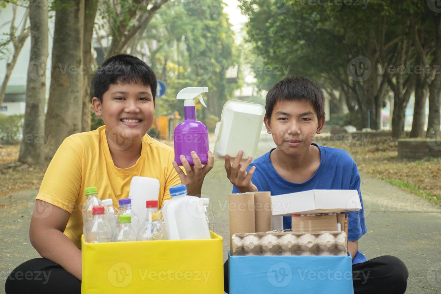 Young asian boy sorting various garbages and putting them into the boxes infront of him in the park, nature care and environment love concept. photo