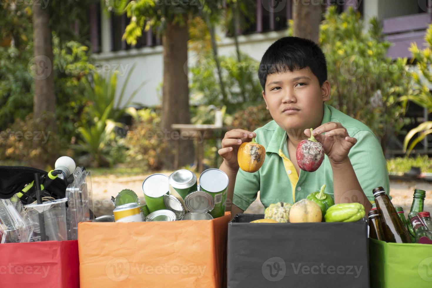 Asian boy is separating garbages and putting them into the boxes in front of him near building, soft and selective focus, environment care, community service and summer vacation activities concept. photo