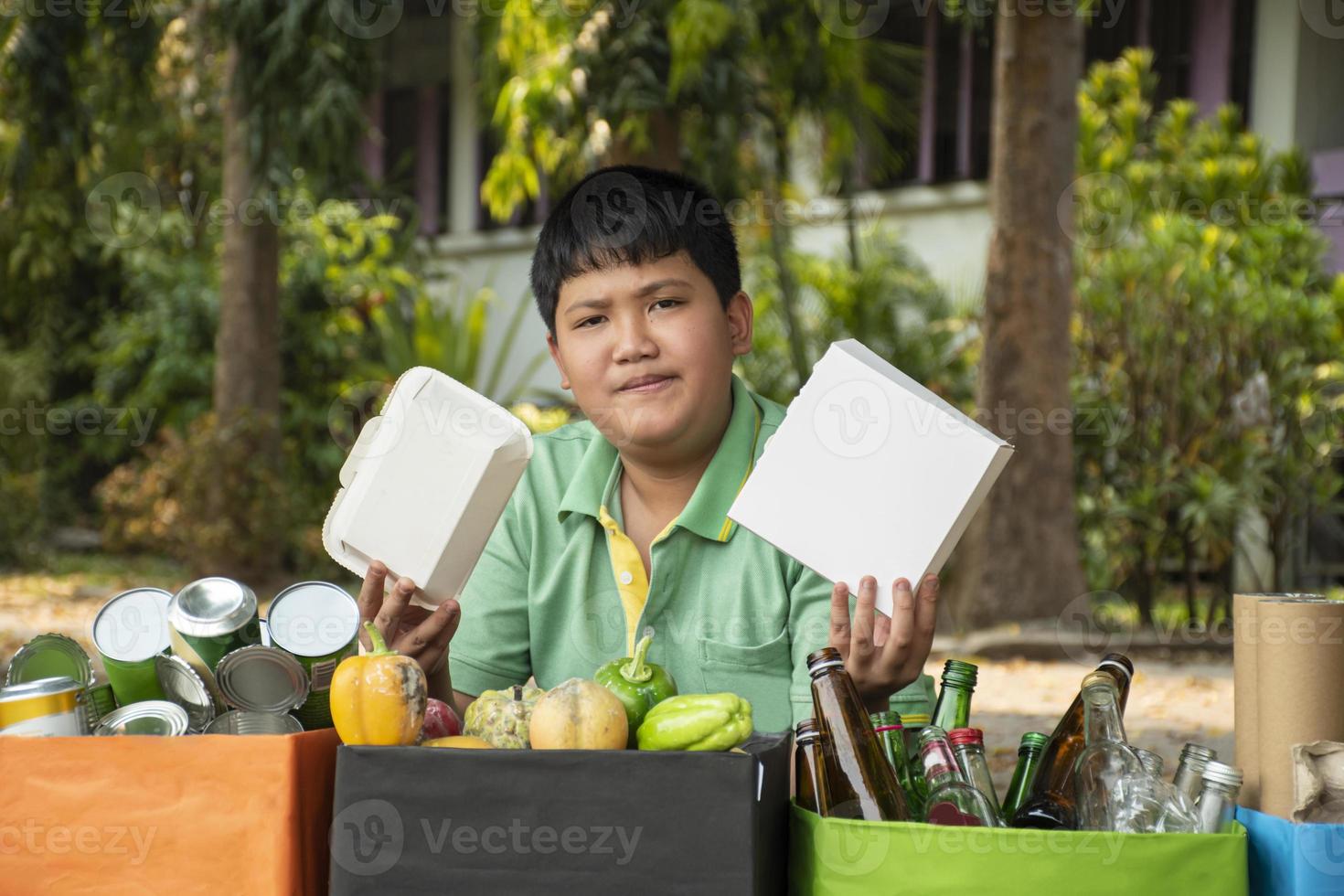 Asian boy is separating garbages and putting them into the boxes in front of him near building, soft and selective focus, environment care, community service and summer vacation activities concept. photo