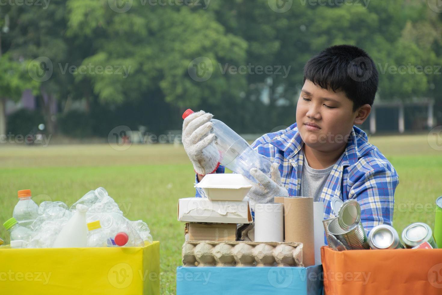 Young asian boy sorting various garbages and putting them into the boxes infront of him in the park, nature care and environment love concept. photo